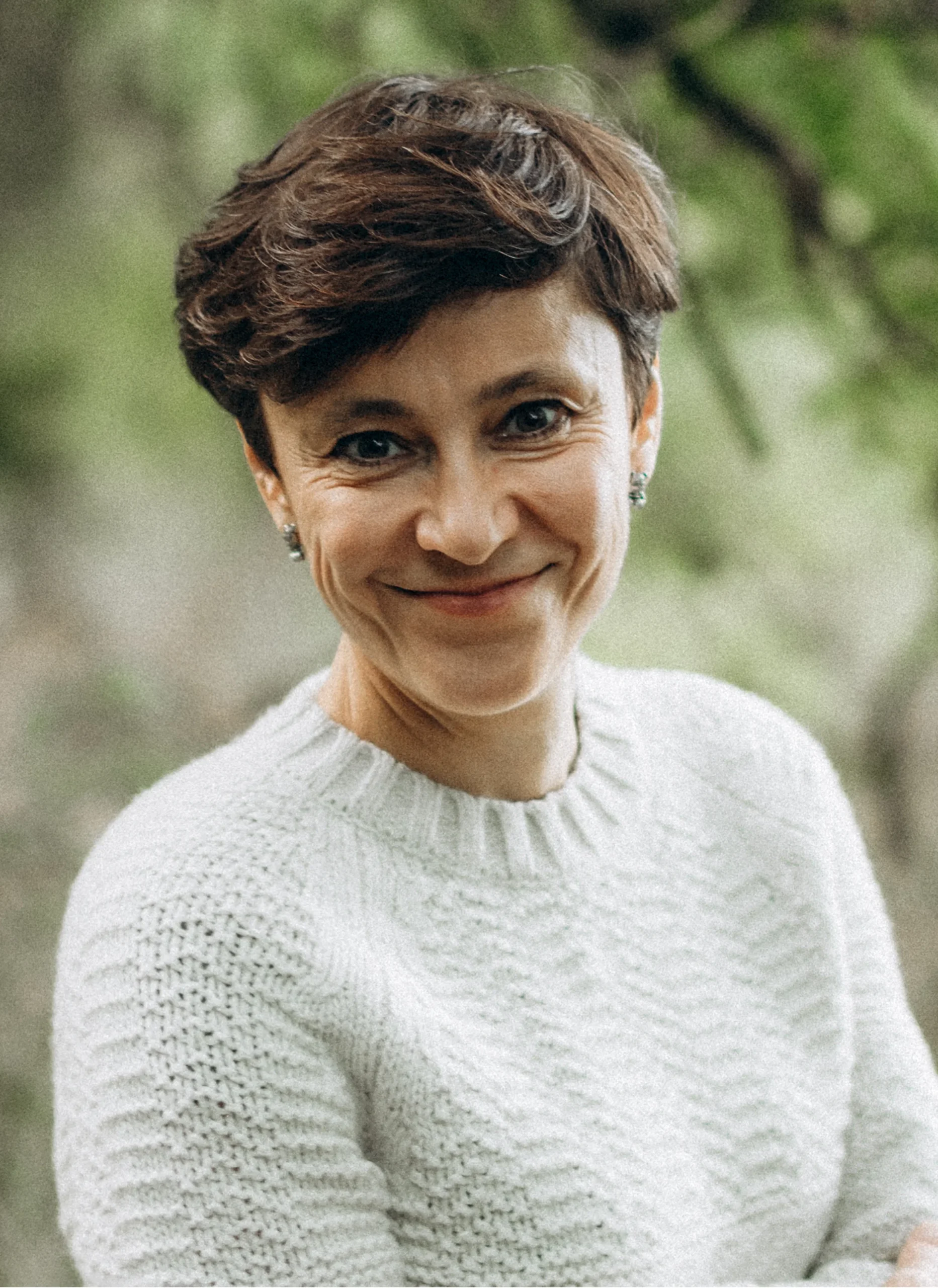 Irina Dmitrieva smiling warmly, wearing a white knitted jumper, photographed outdoors.