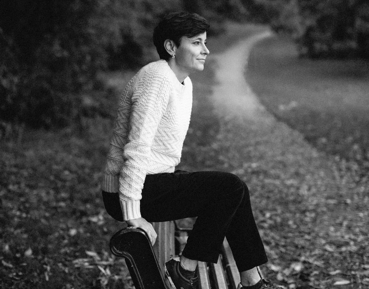 Irina Dmitrieva, career coach, seated on a bench in a park, looking into the distance. A winding path stretches behind her through autumn trees.